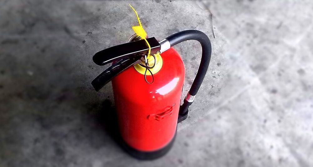 Red fire extinguisher with a black hose on a grey concrete floor